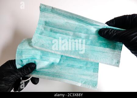 Zwei Hände in schwarzen Handschuhen, die ein Paar Gesichtsmasken auf weißem Hintergrund halten. Virusverbreitung und Bakterienprävention. Sicherheitsmaßnahmen Stockfoto