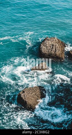 Schönes blaues Meer in Nerja, Spanien. Wellen brechen gegen die Felsen. Kraftvolle stürmische Natur an einem guten Tag bei sonnigem Wetter. Schaum zwischen Steinen Stockfoto