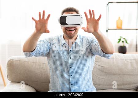 Junger Mann mit Virtual-Reality-Brille, sitzt auf der Couch Stockfoto