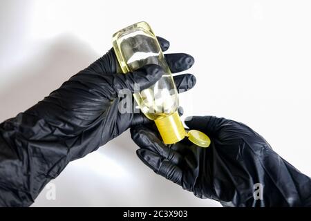 Zwei Hände in schwarzen Handschuhen, die Handdesinfektionsmittel aus einer kleinen gelben Flasche auf weißem Hintergrund auftragen. Desinfizieren von Oberflächen, um in Isolation gesund zu bleiben Stockfoto