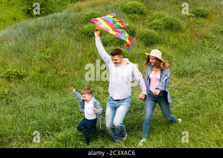 Familie von drei läuft durch Feld mit hellen Drachen in den Händen Stockfoto