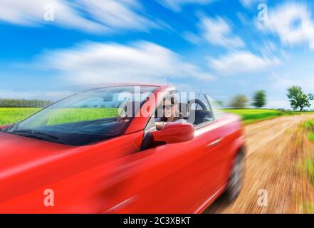 Frau fährt in einem roten Auto auf einer Landstraße. Bewegungseffekt hinzugefügt. Stockfoto