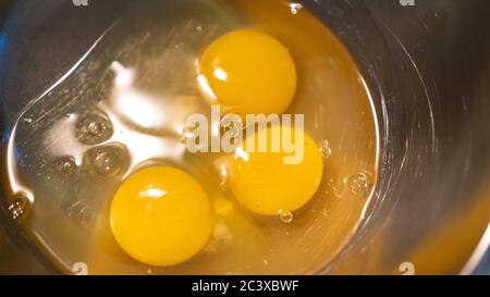Gelbe Eier auf Metallschüssel. Drei Eigelb für Hühnereier. Vorbereitung für Rühreier in einer Metallschüssel. Eier kochen Stockfoto