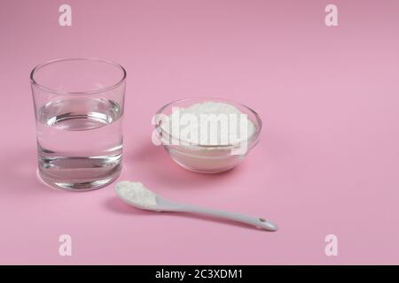 Colagen Pulver in einer Schüssel mit einem Teelöffel und einem Glas Wasser auf einem rosa Hintergrund. Zeit für natürliche Schönheit. Speicherplatz kopieren. Stockfoto