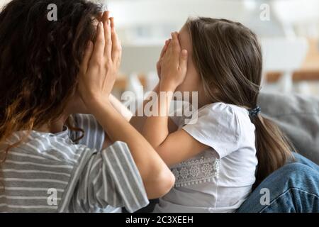 Close up attraktive Mutter spielen mit niedlichen Tochter Abdeckung Gesicht. Stockfoto