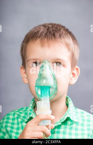 Der Junge macht Inhalation in einer Maske auf grauem Hintergrund Stockfoto