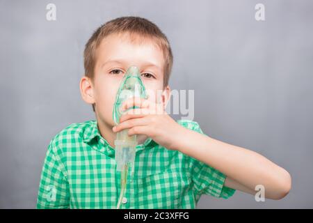 Der Junge macht Inhalation in einer Maske auf grauem Hintergrund Stockfoto