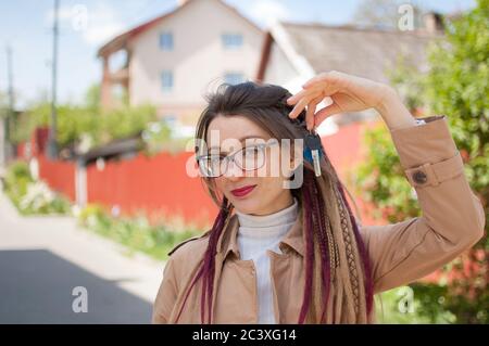 Modernes junges Mädchen mit langen Dreadlocks und Brillen zeigt Haufen Hausschlüssel in einer Hand in Richtung der Kamera. Immobilienmakler Konzept Stockfoto