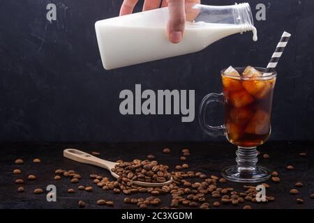 In einem Glas kalten Brühkaffees Milch aus einer Flasche gegossen Stockfoto