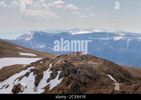 Schöne Aussicht von einem Berg Hügel bedeckt von verbleibendem Schnee Am Ende des Winters und entfernten Berggipfeln unter Ein blauer Himmel Stockfoto