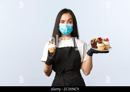 Covid-19, soziale Distanzierung, kleine Coffee-Shop-Geschäft und Prävention Virus Konzept. Fasziniert asiatische weibliche Barista, Kellnerin hält Muffin und schauen Stockfoto