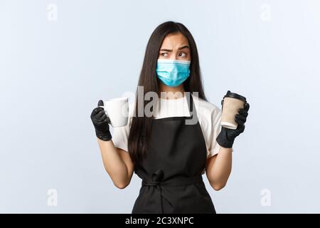 Covid-19, soziale Distanzierung, kleine Coffee-Shop-Geschäft und Prävention Virus Konzept. Asiatische weibliche Barista denken, in welcher Tasse Kaffee regelmäßig oder Stockfoto