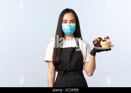 Covid-19, soziale Distanzierung, kleine Coffee-Shop-Geschäft und Prävention Virus Konzept. Attraktive asiatische weibliche Barista, Kellnerin hält Teller mit Stockfoto