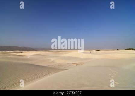 Fußabdrücke im weißen Sand und Menschenfigur weit weg. Aomak Wüste bei Sonnenuntergang, Insel Socotra, Jemen. Das geschützte Gebiet des Aomak Strandes, Golf von Ad Stockfoto