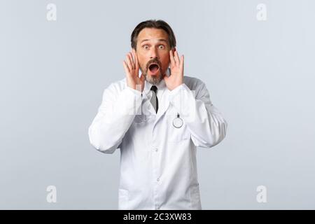 Covid-19, Coronavirus-Ausbruch, medizinisches Personal und Pandemiekonzept. Schockiert aufgeregt männlichen Arzt in weißem Mantel rufen jemanden, laut mit schreien Stockfoto