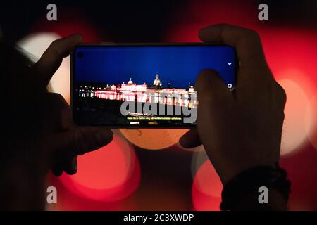 Dresden, Deutschland. Juni 2020. Ein Mann fotografiert mit einem Smartphone die Kunstakademie und Brühls Terrasse, die abends rot beleuchtet sind. Sachsen beteiligt sich an der bundesweiten Kampagne "Nacht des Lichts". In der Nacht zum 23. Juni werden Veranstaltungsorte und ausgewählte Gebäude in ganz Deutschland rot beleuchtet, um auf die dramatische Situation der Corona-Pandemie in der Eventbranche aufmerksam zu machen. Quelle: Sebastian Kahnert/dpa-Zentralbild/dpa/Alamy Live News Stockfoto