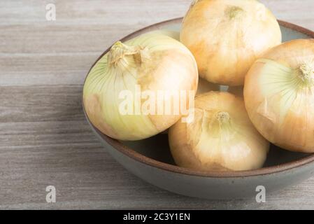 Ein Bündel von authentischen südlichen süßen weißen Zwiebeln kunstvoll auf einer Keramikschale auf einem weiß bemalten rustikalen Holzplatte platziert angeordnet. Stockfoto