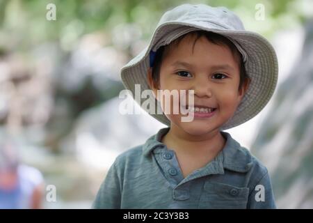 Junge hispanische Junge trägt einen Fischhut, der lächelt und sieht glücklich in einer natürlichen Umgebung im Freien. Stockfoto