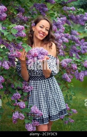 Schöne lockig behaarte Mädchen mit einem Lächeln auf ihrem Gesicht Im blühenden Flieder Stockfoto