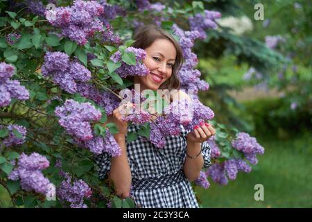 Schöne lockig behaarte Mädchen mit einem Lächeln auf ihrem Gesicht Im blühenden Flieder Stockfoto