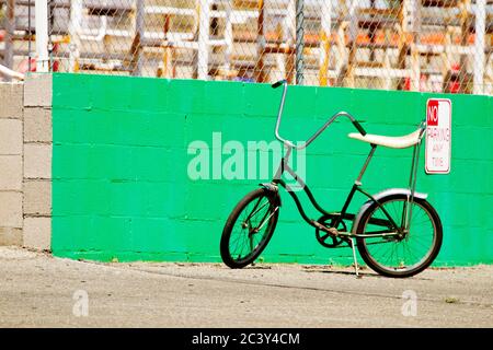 Ein Retro-Fahrrad, das vor einem Schild ohne Parkplatz an einer grünen Wand geparkt ist. Stockfoto