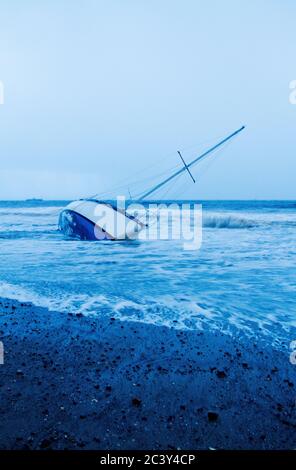 Ein verlassenes kenteres Boot im Meer nach einem Sturm. Stockfoto