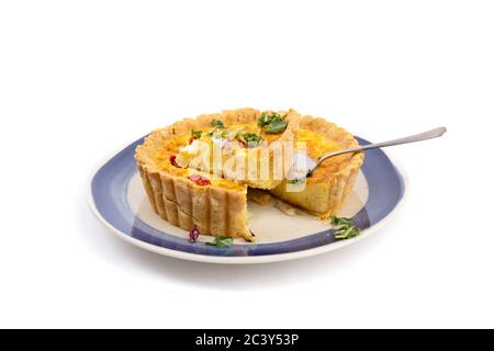 Eine Käsequiche mit getrockneten Tomaten mit einem Stück ausgeschnitten bereit zu servieren isoliert auf weiß Stockfoto