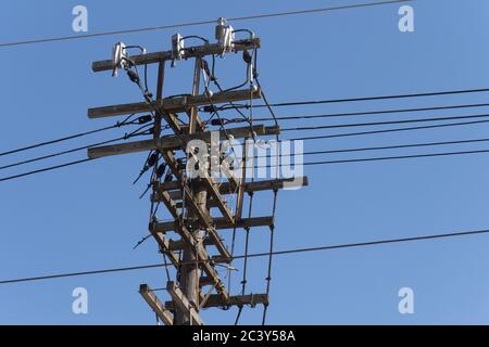 Ein alter hölzerner elektrischer Strommast mit einem Durcheinander von Drähten und Isolatoren auf einem blauen Himmel Stockfoto