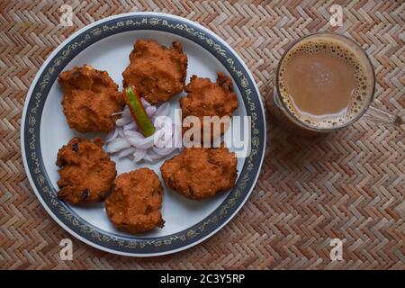 Draufsicht auf Dal vada, Masala vada, Chana vada serviert mit geschnittenen Zwiebeln und grünem Chilly und Tee auf Serviermatte. Frittierte indische Küche Snacks, Linsen Stockfoto