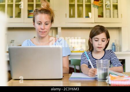 Frau, die am Laptop arbeitet und Mädchen (6-7), die Hausaufgaben machen Stockfoto