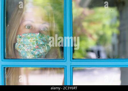 Frau in Gesichtsmaske Blick durch Fenster Stockfoto