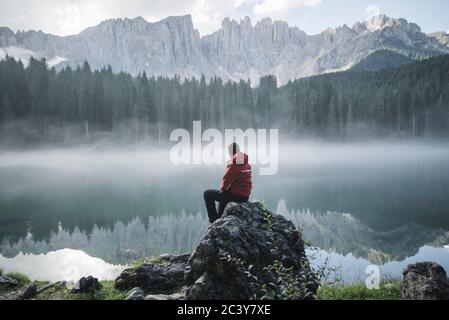 Schweiz, junger Mann sitzt am Karersee in den Dolomitenalpen im Morgengrauen Stockfoto