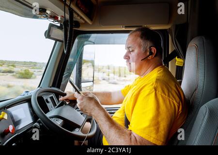 Fahrer in der Kabine auf der Autobahn des Smartphones in der Hand des Menschen sitzen hinter dem Steuer des großen modernen LKW-Fahrzeug Stockfoto