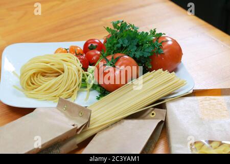 Ungekochte Nudeln in einer Papierverpackung mit frischen Tomaten und Sellerie. Frische Spaghetti-Zutaten. Stockfoto