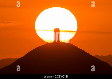 Glastonbury, Somerset, Großbritannien. Juni 2020. Wetter in Großbritannien. Die Sonne geht hinter dem Glastonbury Tor in Somerset auf, das im hellorangen Himmel bei Sonnenaufgang dargestellt wird. Bildquelle: Graham Hunt/Alamy Live News Stockfoto