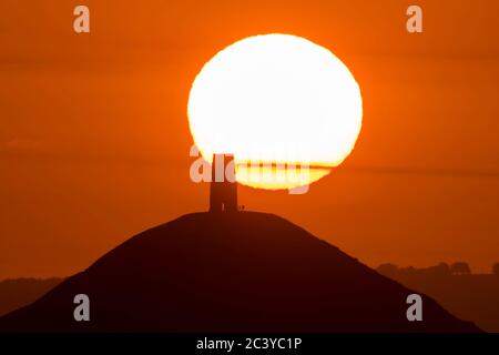 Glastonbury, Somerset, Großbritannien. Juni 2020. Wetter in Großbritannien. Die Sonne geht hinter dem Glastonbury Tor in Somerset auf, das im hellorangen Himmel bei Sonnenaufgang dargestellt wird. Bildquelle: Graham Hunt/Alamy Live News Stockfoto