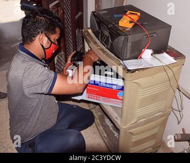 Ein indischer Elektriker repariert eine defekte Inverterbatterie, während er eine Gesichtsmaske trägt, um Covid 19 während der Sperre zu verhindern Stockfoto