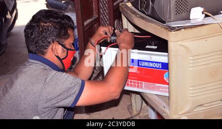 Nahaufnahme eines indischen Elektrikers, der eine Batterie mit Inverter-Blei repariert und gleichzeitig eine Schutzmaske trägt, um bei der Sperrung das Corona-Virus zu verhindern Stockfoto