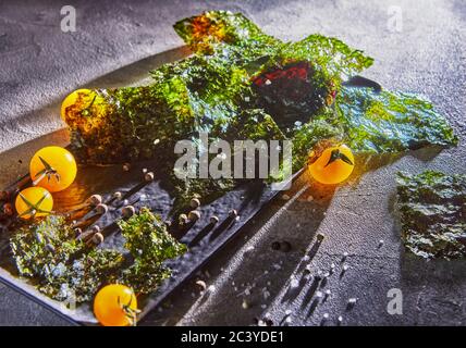 Knusprige Nori-Algen mit Kirschtomaten und dunklen Gewürzen auf grauem Beton. Japanisches Essen Nori. Getrocknete Blätter von Algen. Speicherplatz kopieren. Stockfoto