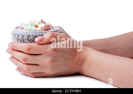 Heißes Getränk und mehrfarbige Marshmallows in einem Becher in Frauenhänden, eingewickelt in einen gestrickten Getränkehalter isoliert auf weißem Hintergrund Stockfoto