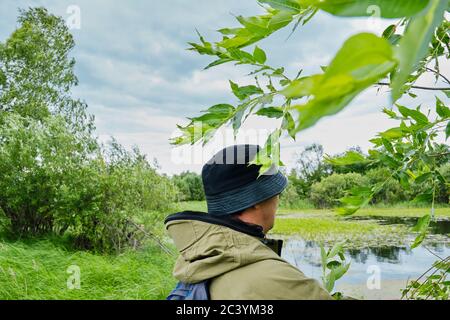 Aktiver Mann in Moskitoanzug mit Rucksack beim Wandern in der Nähe Waldsee in sibirien, russland. Alleinreisen, Lifestyle, inländisches Tourismuskonzept Stockfoto