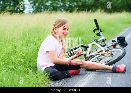 Trauriger weinender kleiner Kindermädchen fiel vom Fahrrad im Sommerpark. Blutungen an Händen und Füßen. Fahrradunfall. Verletzungen beim Radfahren. Stockfoto