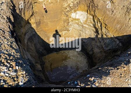 Baugrube mit Grundwasser und Schatten eines Mannes in Sonnenschein Stockfoto