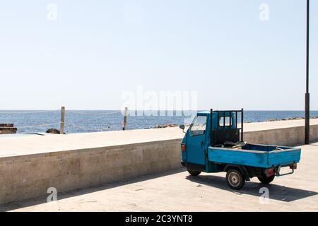 Blaues Dreirad am Hafen in Meeresnähe. Typische Transport- und Arbeitsmittel Stockfoto