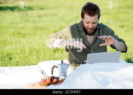 Mann niesen während er an seinem Laptop arbeitete, im Bett im Freien in grassfield sitzend Stockfoto