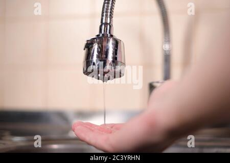 Ein Mann öffnet einen Wasserhahn in der Küche, aber kein Wasser kommt. Überlappendes Wasser Stockfoto