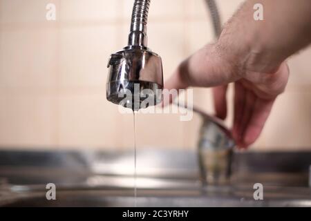 Ein Mann öffnet einen Wasserhahn in der Küche, aber kein Wasser kommt. Überlappendes Wasser Stockfoto