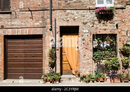 Typische Fassade eines Hauses in einem kleinen italienischen Dorf mit Ziegelmauer, hölzernen Eingang und blühenden Pflanzen in Töpfen Stockfoto