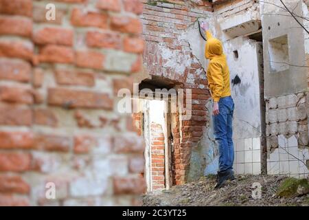 Junger Kerl zeichnet Sprühfarbe an der Wand eines Verlassene Gebäude Stockfoto