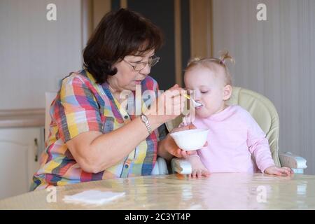 Großmutter füttert ihre Enkelin mit einem Löffel. Das Mädchen frisst Stockfoto